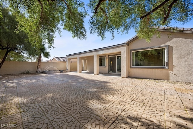 rear view of house featuring stucco siding, fence, and a patio