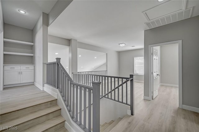 hallway with light wood-style flooring, an upstairs landing, and baseboards