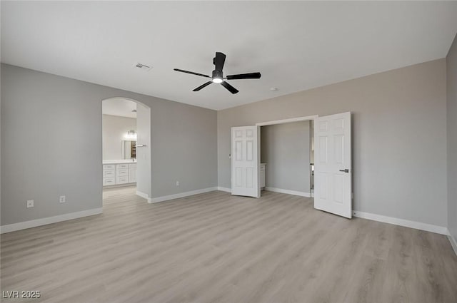 unfurnished bedroom with arched walkways, visible vents, light wood finished floors, and baseboards