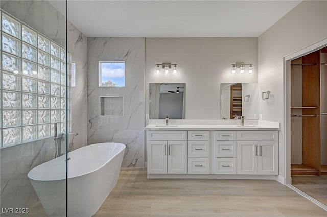 full bathroom featuring a freestanding tub, double vanity, a sink, and wood finished floors