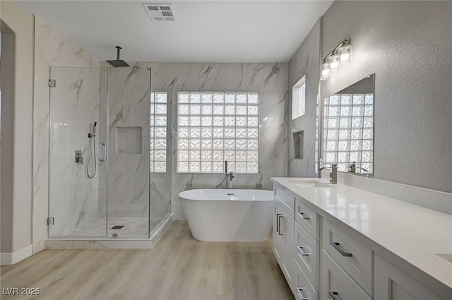 full bath featuring a freestanding bath, a marble finish shower, visible vents, and wood finished floors