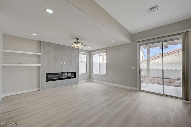 unfurnished living room with baseboards, visible vents, wood finished floors, and a tile fireplace