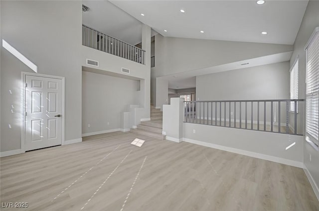 unfurnished living room with high vaulted ceiling, recessed lighting, light wood-style flooring, and baseboards