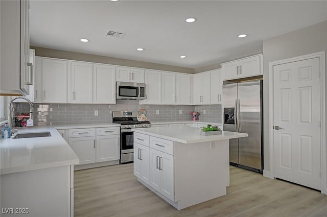 kitchen featuring light wood-style flooring, appliances with stainless steel finishes, white cabinets, and a sink