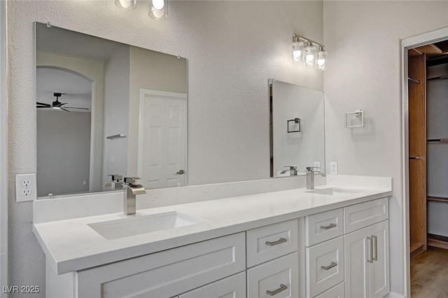 bathroom with ceiling fan, double vanity, wood finished floors, and a sink