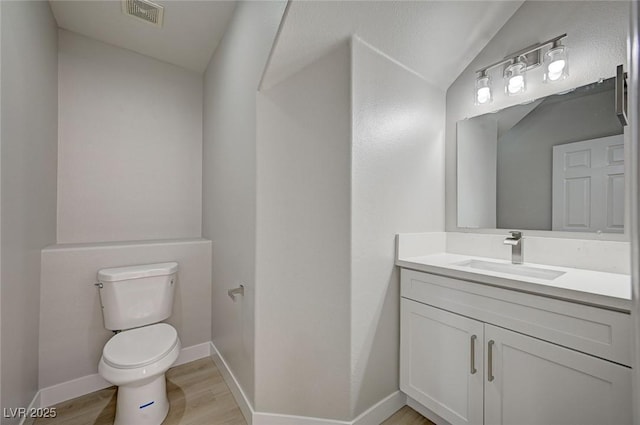 half bathroom featuring visible vents, toilet, vanity, wood finished floors, and baseboards