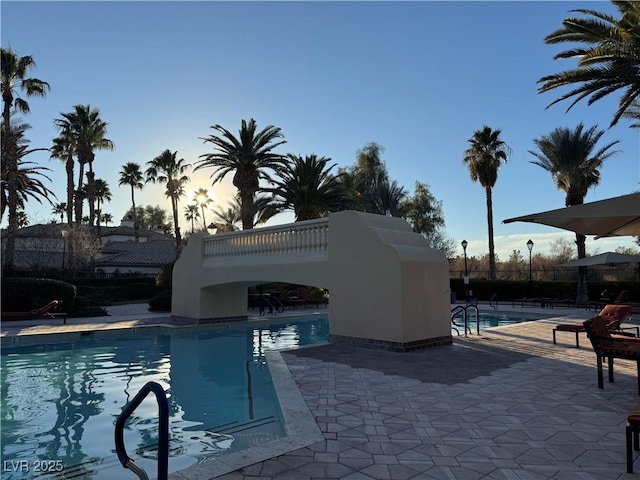 pool at dusk featuring a patio area and a community pool