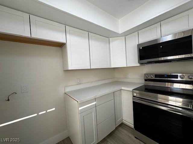 kitchen with light countertops, appliances with stainless steel finishes, white cabinets, wood finished floors, and baseboards