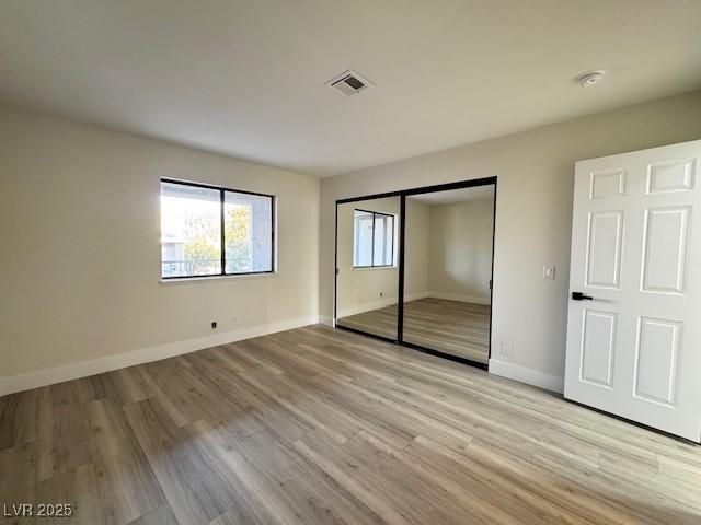 unfurnished bedroom featuring visible vents, a closet, light wood-style flooring, and baseboards