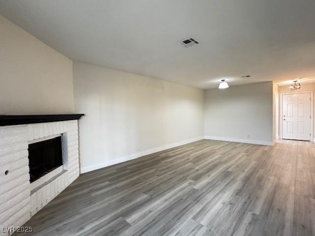 unfurnished living room featuring baseboards, a fireplace, visible vents, and wood finished floors