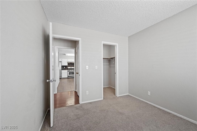 unfurnished bedroom featuring a textured ceiling, baseboards, a closet, carpet, and a walk in closet