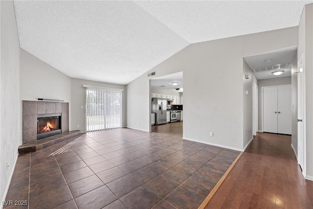 unfurnished living room featuring lofted ceiling, visible vents, a tiled fireplace, a textured ceiling, and baseboards