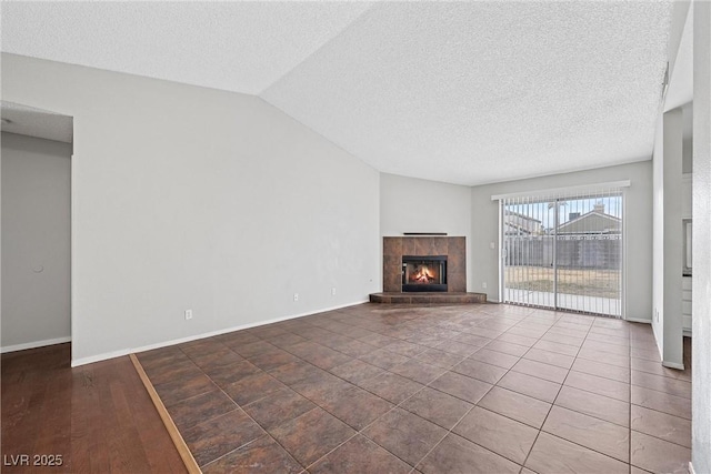 unfurnished living room with baseboards, vaulted ceiling, a textured ceiling, and a tiled fireplace