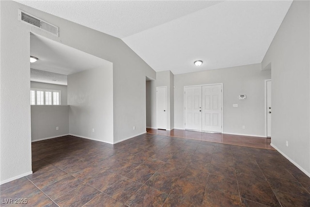 empty room with vaulted ceiling, a textured ceiling, visible vents, and baseboards