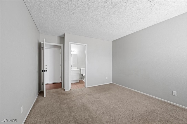 unfurnished bedroom featuring a textured ceiling, carpet, connected bathroom, and baseboards