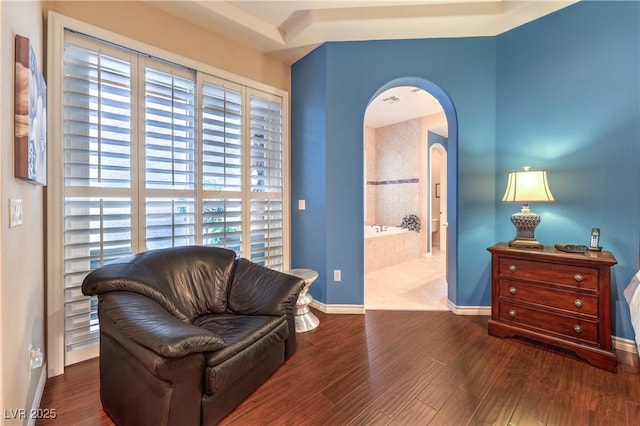 sitting room featuring arched walkways, baseboards, and wood finished floors