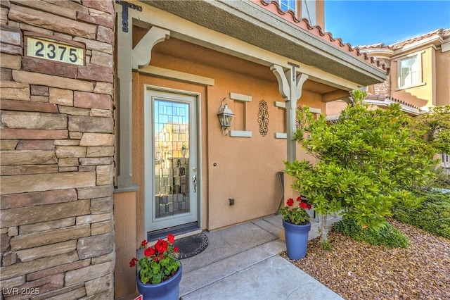 doorway to property featuring stone siding, a tiled roof, and stucco siding