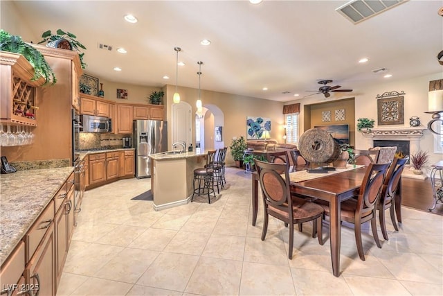 dining room with light tile patterned floors, arched walkways, a ceiling fan, a fireplace, and recessed lighting