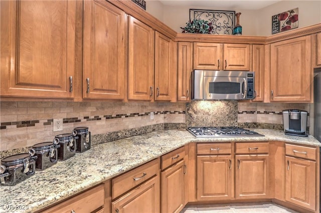 kitchen featuring light stone countertops, appliances with stainless steel finishes, brown cabinets, and backsplash