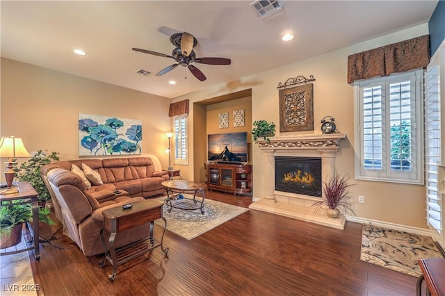 living area with ceiling fan, wood finished floors, a glass covered fireplace, and visible vents