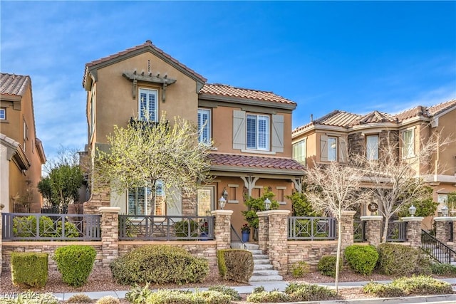 mediterranean / spanish house with a tile roof, stucco siding, a porch, fence, and stone siding