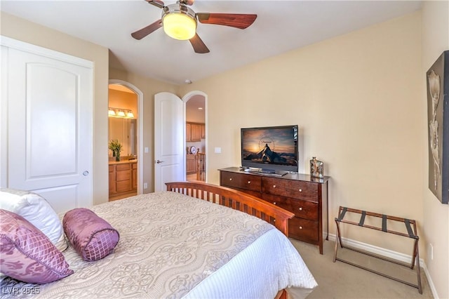 bedroom with baseboards, arched walkways, connected bathroom, light colored carpet, and ceiling fan