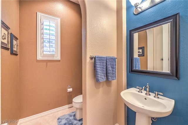 half bath with baseboards, a sink, toilet, and tile patterned floors