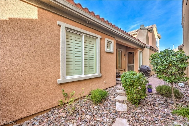 view of side of home featuring a patio area, a tile roof, and stucco siding