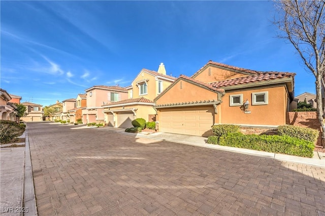 mediterranean / spanish-style house with decorative driveway, stucco siding, a garage, a residential view, and a tiled roof