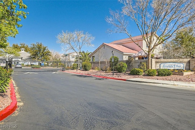 view of street featuring a gated entry, curbs, a residential view, a gate, and street lighting