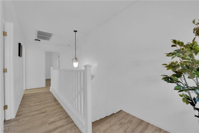 corridor with light wood-style floors, visible vents, and an upstairs landing