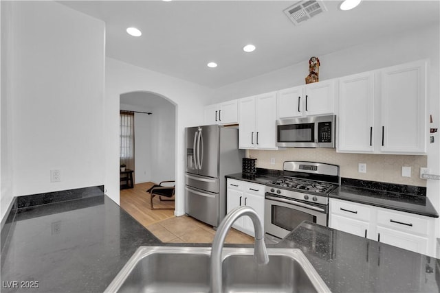 kitchen with arched walkways, visible vents, appliances with stainless steel finishes, white cabinetry, and a sink