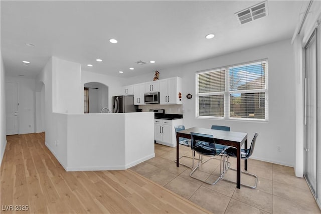 kitchen with visible vents, arched walkways, stainless steel appliances, white cabinetry, and recessed lighting