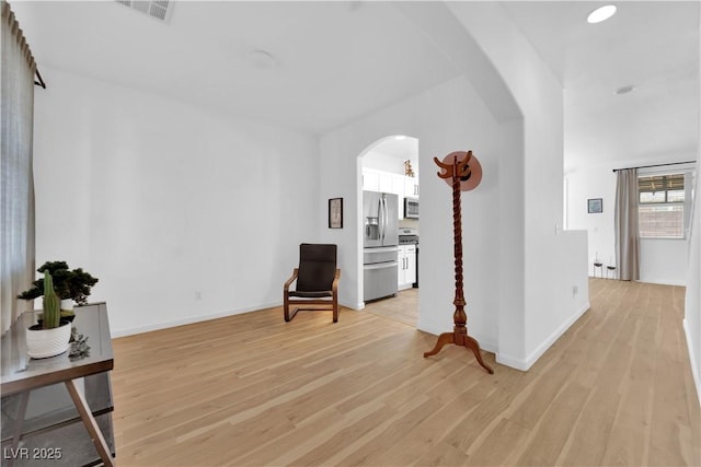 living area with arched walkways, baseboards, visible vents, and light wood finished floors