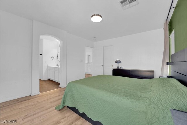 bedroom featuring light wood finished floors, visible vents, arched walkways, and connected bathroom