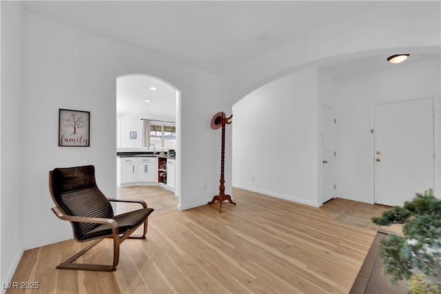 living area featuring light wood finished floors, baseboards, and arched walkways