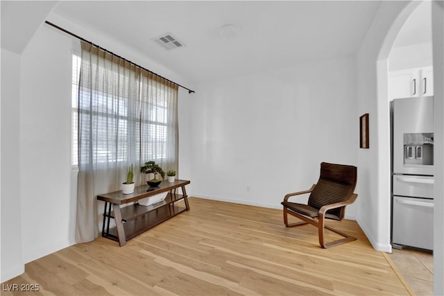 sitting room with arched walkways, light wood-style flooring, visible vents, and baseboards