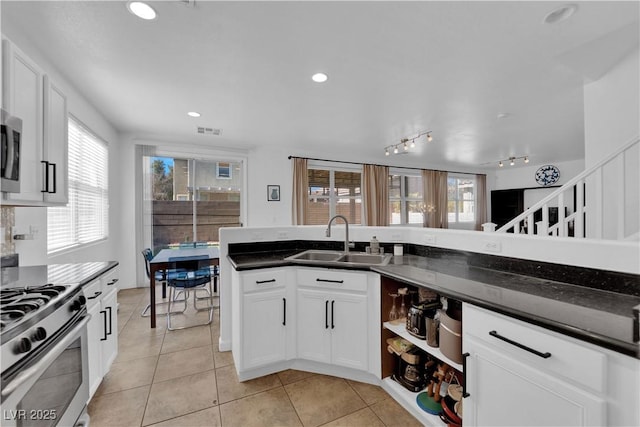 kitchen with stainless steel gas stove, light tile patterned floors, visible vents, dark countertops, and a sink