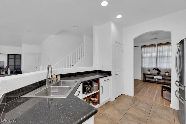 kitchen featuring arched walkways, recessed lighting, freestanding refrigerator, light tile patterned flooring, and a sink