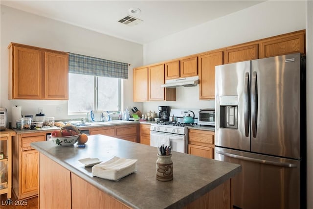 kitchen with under cabinet range hood, a sink, visible vents, white gas range oven, and stainless steel refrigerator with ice dispenser