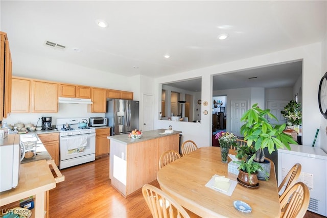 kitchen featuring white gas stove, light brown cabinets, under cabinet range hood, visible vents, and stainless steel refrigerator with ice dispenser