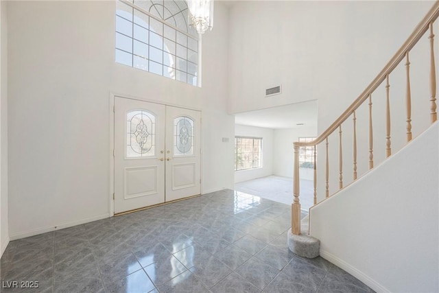 tiled entrance foyer with a towering ceiling, baseboards, stairs, visible vents, and an inviting chandelier