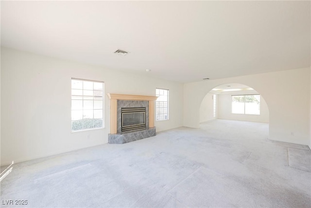 unfurnished living room with arched walkways, visible vents, a fireplace, and light carpet