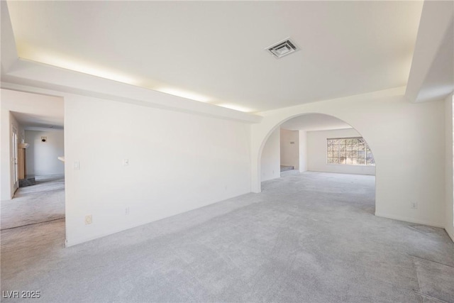 unfurnished room featuring light carpet, a raised ceiling, arched walkways, and visible vents