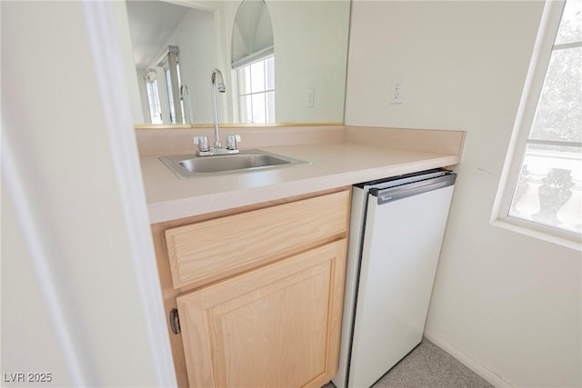 kitchen with a sink, baseboards, light countertops, dishwasher, and light brown cabinetry