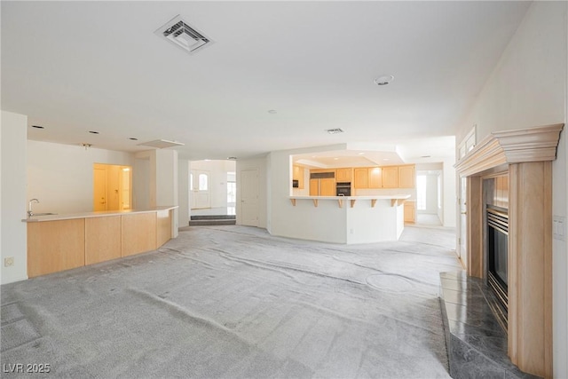 unfurnished living room featuring light carpet, a sink, visible vents, and a wealth of natural light