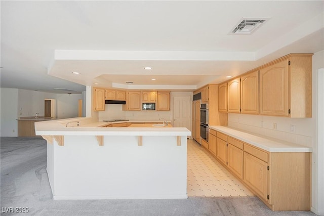 kitchen featuring visible vents, a raised ceiling, a breakfast bar, black appliances, and light brown cabinets