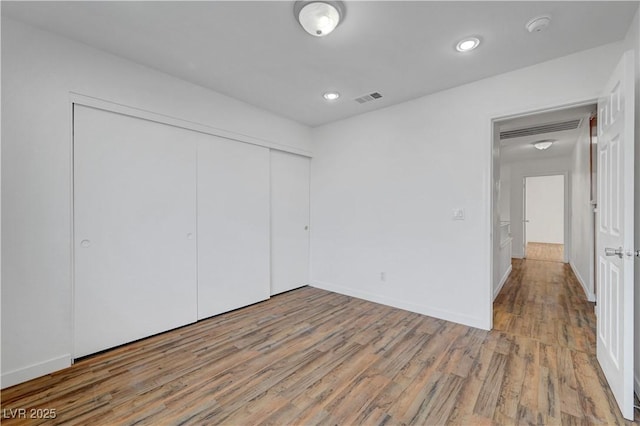 unfurnished bedroom featuring baseboards, a closet, visible vents, and wood finished floors