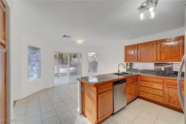 kitchen featuring visible vents, stainless steel dishwasher, brown cabinetry, a sink, and a peninsula