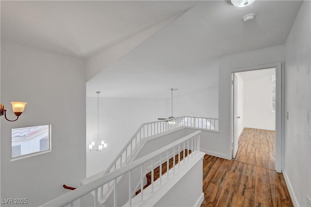 hallway featuring wood finished floors, baseboards, an upstairs landing, and an inviting chandelier